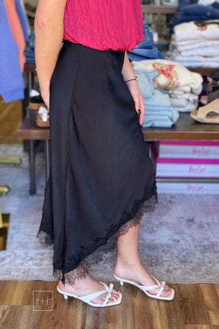Side view of black satin asymmetrical midi skirt with scalloped lace trim, style SKS16677