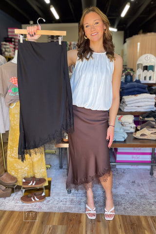 Model wearing chocolate brown satin lace trim midi skirt and holding the black version on a hanger, style SKS16677