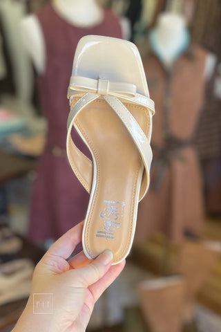 Top view of Corkys Dainty ivory patent sandal showing square open toe, bow detail, and lightly padded footbed, held in hand