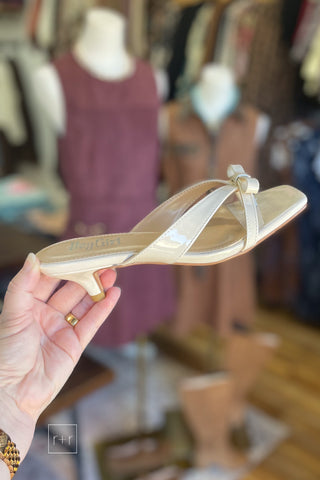 Side view of Corkys Dainty ivory patent kitten heel sandal with square toe and bow detail, held in hand