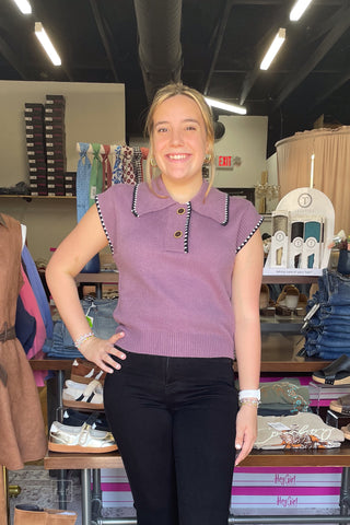 Dusty plum knit polo sweater with black and white contrast stitch trim on the collar and cap sleeves, worn with black pants.