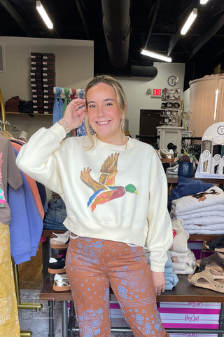 Smiling model in the Poppy & Pine Flying Mallard ivory crop sweatshirt, styled with Poppy & Pine brown Bandana Fray Hem Denim