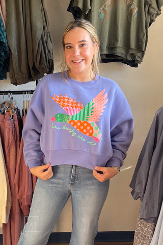 Smiling model wearing the Poppy & Pine How Ducky Are We purple crop sweatshirt with a colorful patchwork mallard graphic