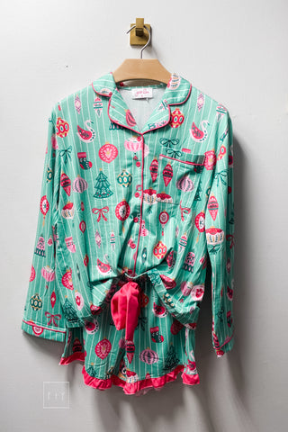 Jess Lea Decked In Ornaments ruffle pajama set in mint green with white pinstripes and a pink, red, and green Christmas ornament print, featuring a long sleeve button-down top with pink piping and matching shorts with a pink ruffle hem, shown on a wooden hanger