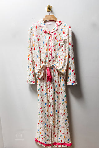 Jess Lea Wrapped in Lights Ruffle Pajama Set in cream with multicolor Christmas string light print, pink piping, long sleeve button-down top and ruffle hem pants on a hanger