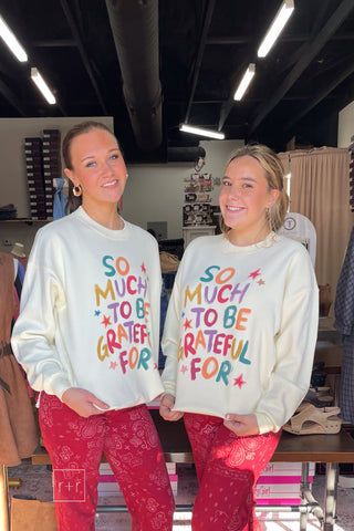 Full-length mirror view of two models in the Poppy & Pine So Much To Be Grateful For oversized ivory sweatshirt, styled with red flare jeans