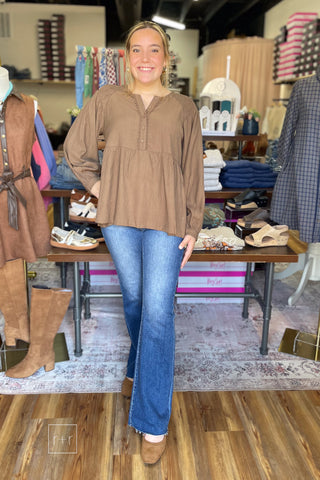 Model standing in the Umgee N7223 almond brown babydoll top with smocked puff sleeves, Risen high rise flare jeans, and Corkys Layover ballet flats in camel