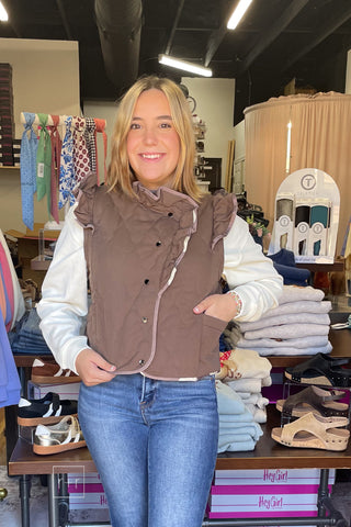 Close front view of the Umgee C6829 mocha quilted vest showing ruffle trim, contrast piping, and snap buttons over the Wishlist Howdy graphic sweatshirt