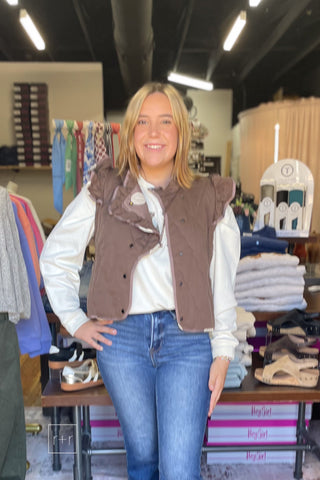 Woman wearing the Umgee C6829 reversible quilted ruffle vest in mocha over the Wishlist Howdy floral graphic sweatshirt WL26-12822 with Risen High Rise Flare Jeans PF21438