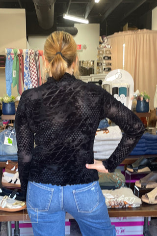 Back view of the Umgee D1256 black velvet burnout mock neck top showing the sheer dot and wave pattern, hand on hip