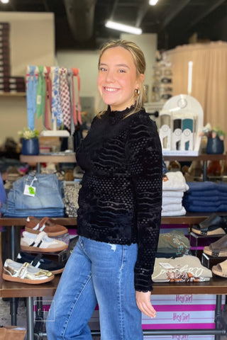 Side view of the Umgee D1256 black velvet burnout mock neck top with lettuce-edge cuffs, worn with Risen High Rise Wide Leg Jeans