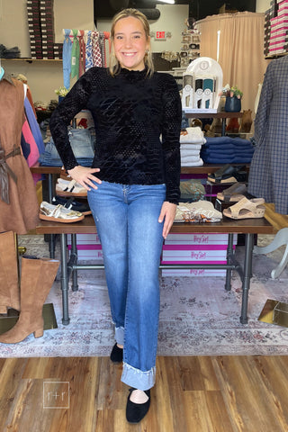 Full-length front view of the Umgee D1256 black velvet burnout mock neck top styled with Risen High Rise Wide Leg Jeans With Wide Cuff and black Corkys Layover Ballet Flats
