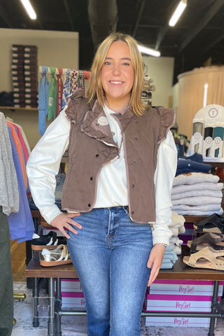 Close front view of the Umgee C6829 mocha quilted vest showing ruffle trim, contrast piping, and snap buttons over the Wishlist Howdy graphic sweatshirt